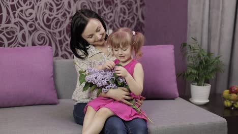 pequeña hija y madre sentadas en el sofá con un ramo de flores púrpuras de lila
