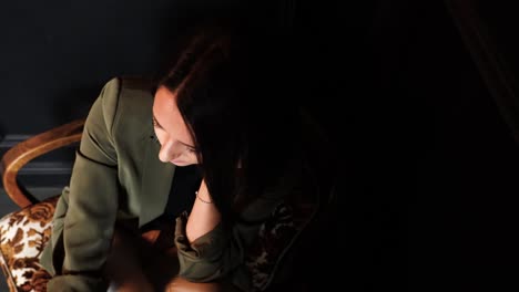 Lonely-and-thoughtful-caucasian-woman-sit-on-armchair-in-dark-wall-room