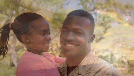 Animation-of-trees-over-happy-african-american-male-soldier-carrying-his-daughter