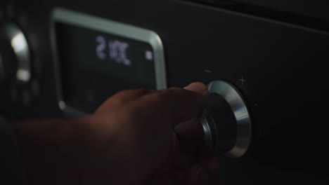 person hand rising temperature of oven using knob, close up view