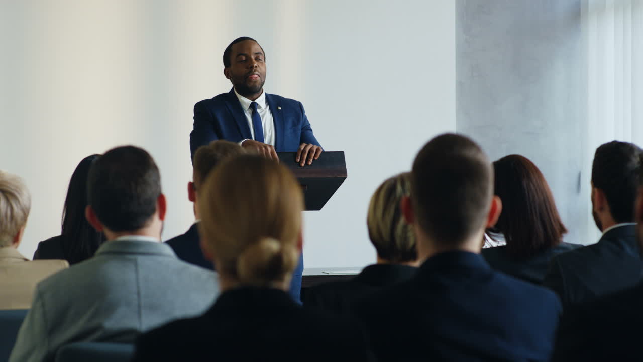 African American businessman speaker on a podium at a conference and interacting with people in the hall during his speech