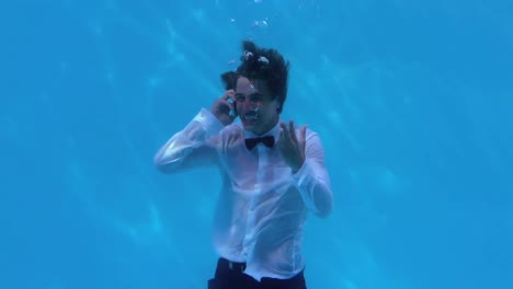 cheering businessman underwater in pool talking on smartphone