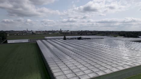 Aufsteigende-Luftbewegung-Zeigt-Gewächshaus-Mit-Antlitz-Stadtbild-Von-Zutphen-Im-Hintergrund-Mit-Kumuluswolken-Vor-Blauem-Himmel-Darüber