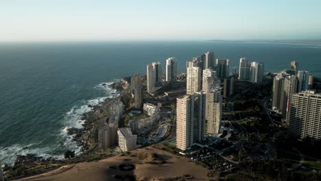 Aerial-orbit-of-buildings-next-to-dunes-in-concon-chile-at-sunset