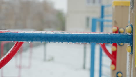 close-up of blue rope attached to yellow ice-coated surface, highlighting fine details of winter frost and blurred playground structures in the background