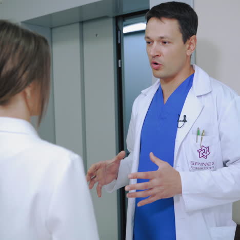 woman doctor is telling seriously to a male doctor as they walk through the private clinic. doctors in medical uniform discussing the health problem while coming to the lift in hospital.