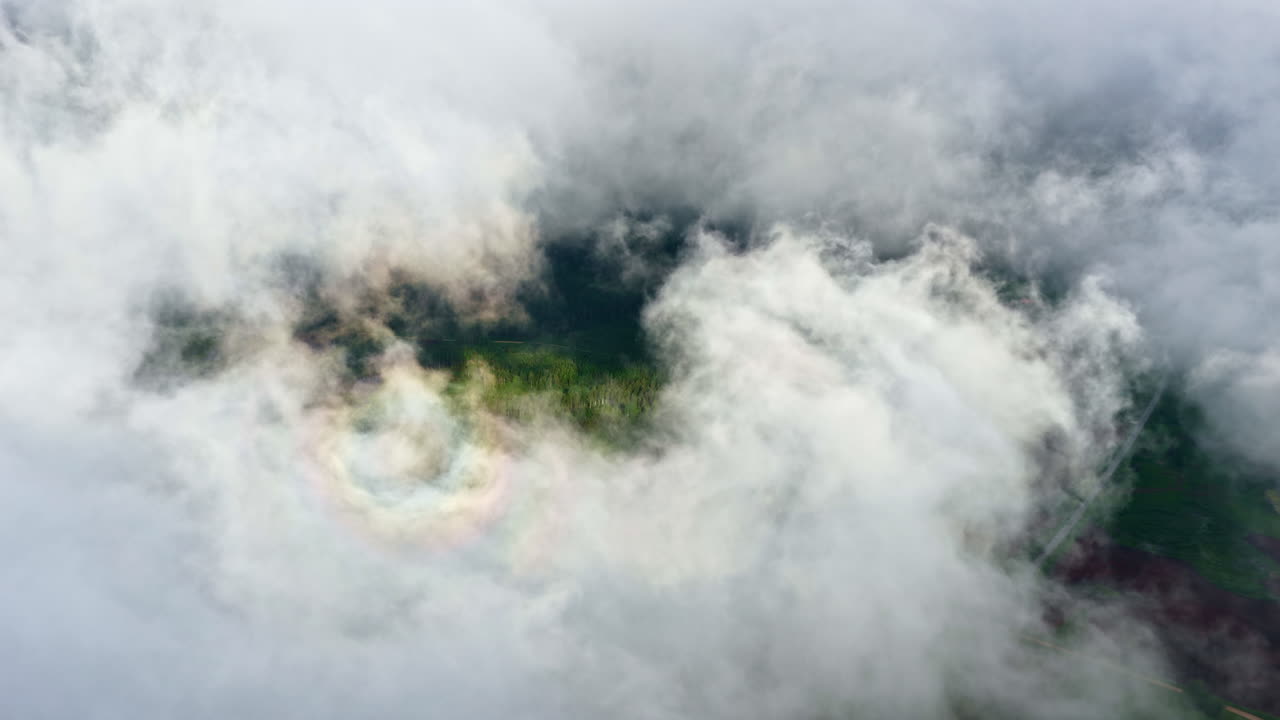 Flying looking straight down through a natural window in a thick blanket of clouds, offering a tantalizing glimpse of the green Latvian countryside hidden below, - cinematic drone shot