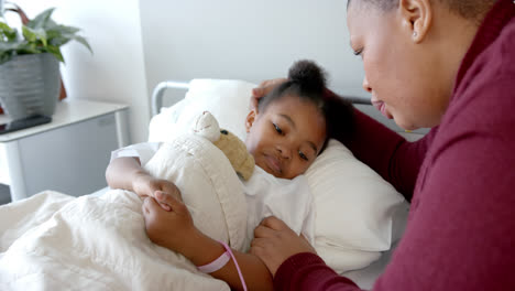 african american mother embracing daughter lying in hospital bed with mascot, slow motion