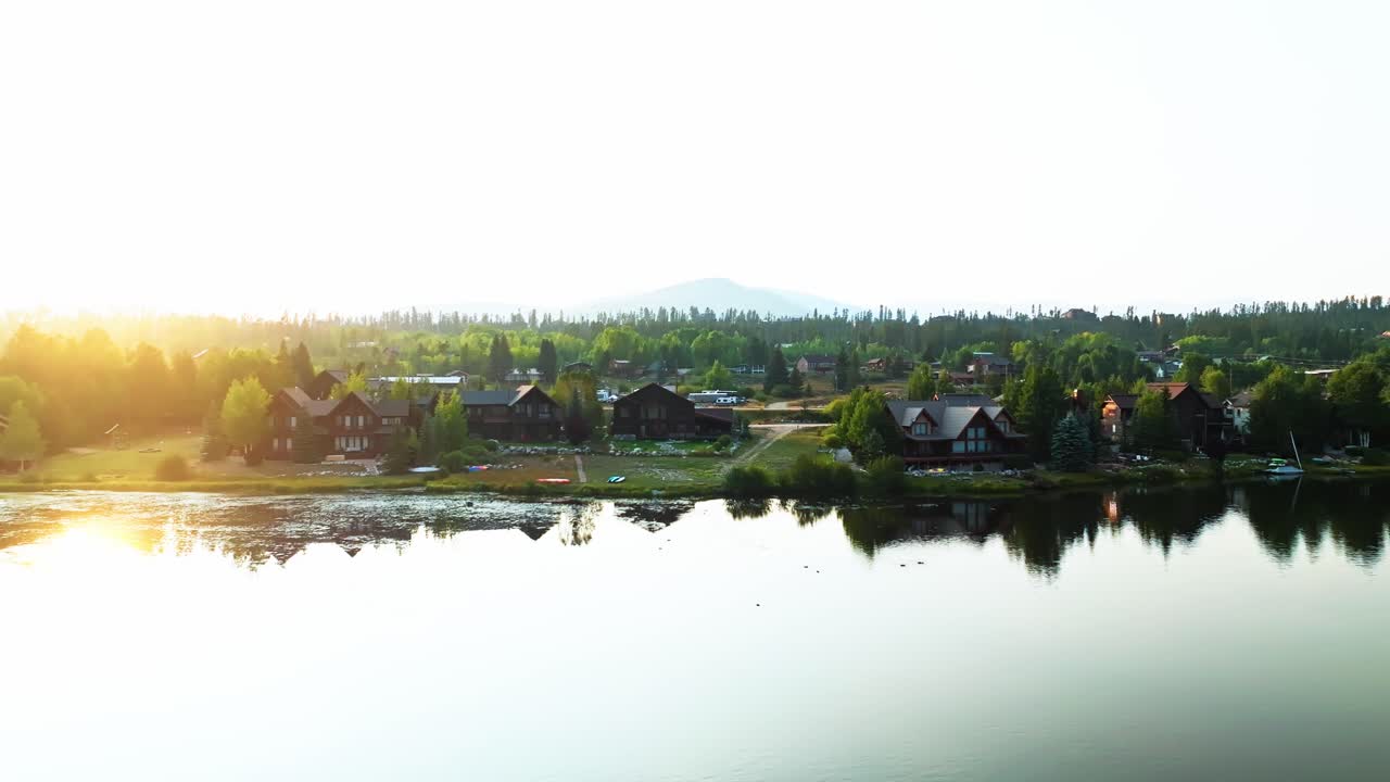 Early morning glow over Grand Lake Colorado with mountains and forests reflected on calm surface, aerial approach to villa homes
