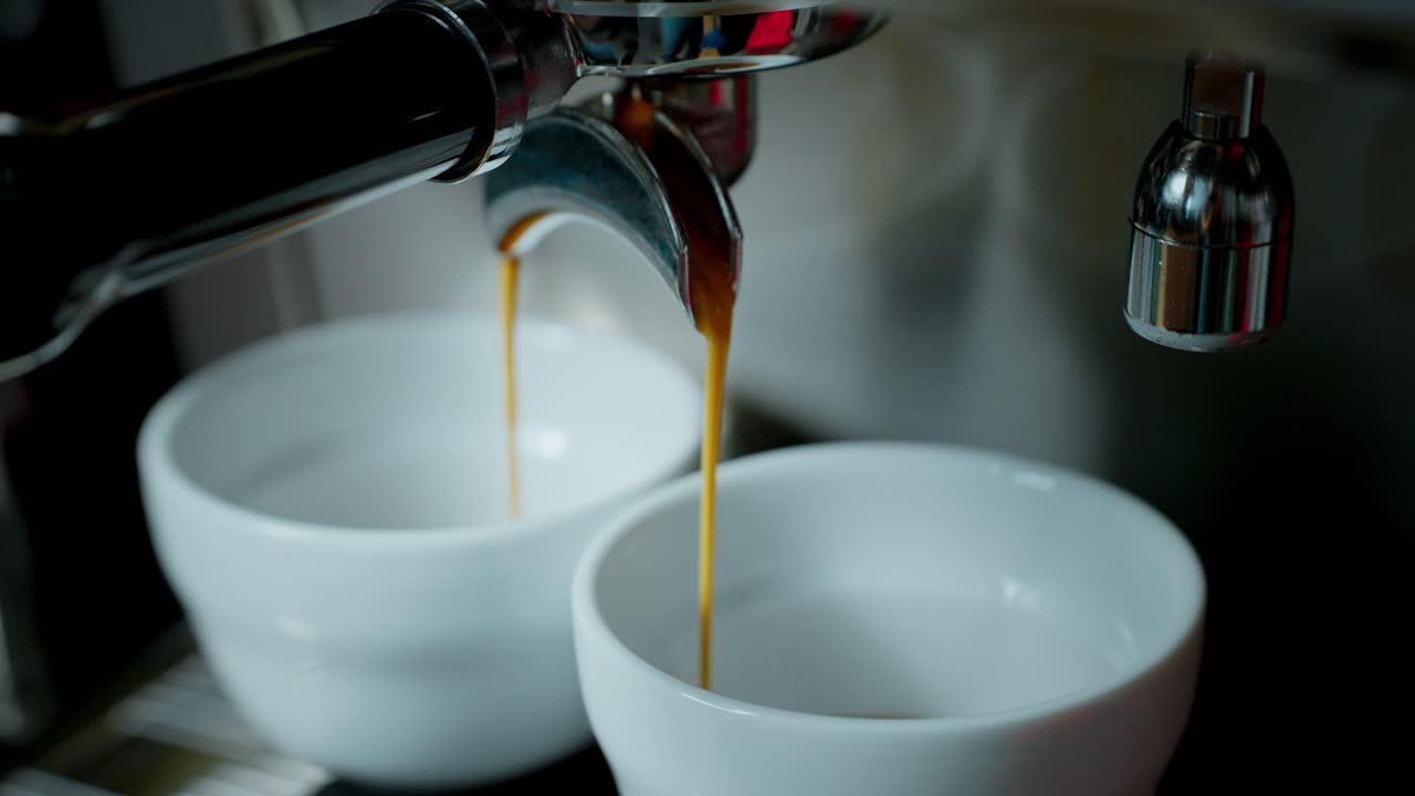 Macchina da caffè espresso che eroga caffè in due tazze bianche.