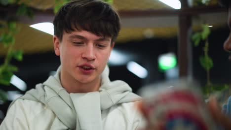 front view white teenager uttering words while looking at companion phone and shaking head in disagreement, facial expression showing doubt and tension during casual indoor meeting