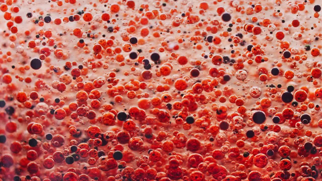 많은 붉은 색과 어두운 거품의 매크로 샷이 천천히 물속에서 땅으로 떨어지고 있습니다.