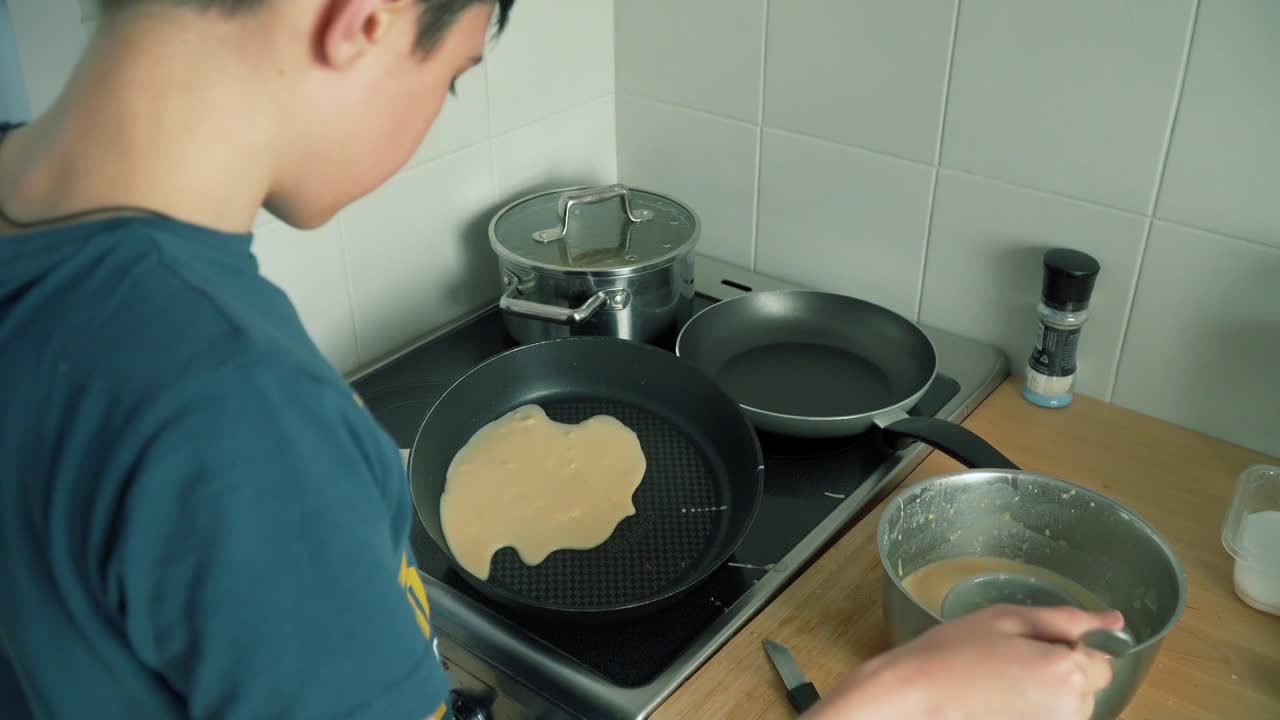 소년은 집에서 부에서 달하고 맛있는 팬케이크를 요리하고 있습니다.