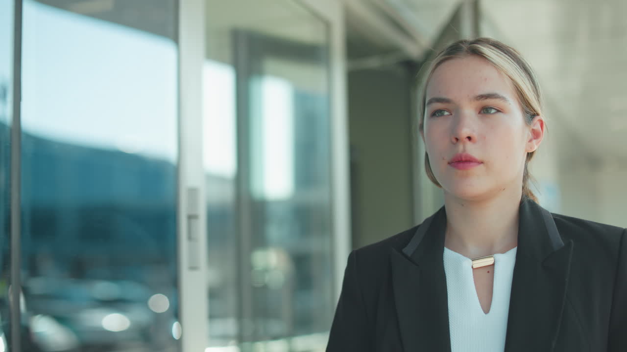Elegant businesswoman exits modern office building after meeting, reflecting on discussion, with urban cityscape mirrored in glass, dressed in professional attire
