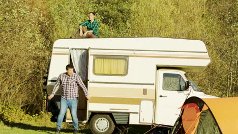 young girl relaxing on top of retro camper van in mountain wilderness