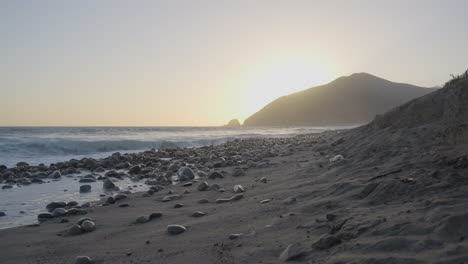 Ascending-shot-of-Mondo's-Beach-shore-as-the-sun-begins-to-set-behind-a-mountain-located-in-Southern-California