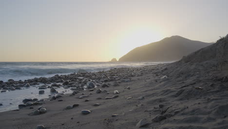 ascending shot of mondo's beach shore as the sun begins to set behind a mountain located in southern california