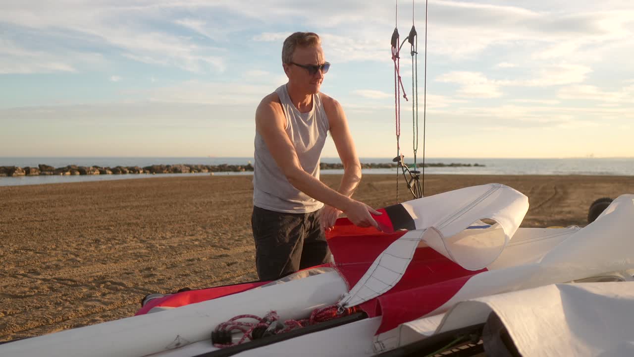 hombre recogiendo las velas de un catamarán en la playa