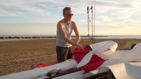 man gathering the sails of a catamaran on the beach