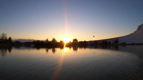 lapso de tiempo de una puesta de sol que se refleja en el lago con un globo de aire caliente volando sobre el cielo - pamukalle, turquía