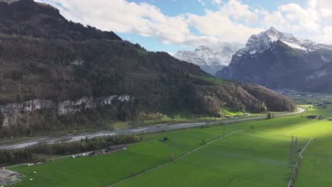 Aerial-shot-of-a-lush-green-valley-near-Weesen,-Switzerland,-with-a-mountain-backdrop-and-a-highway