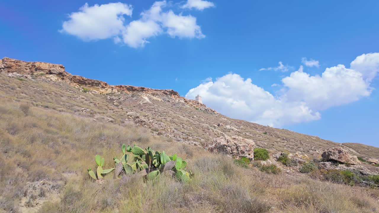 A leisurely exploratory walk near Gnejna Bay, Mgarr, among the dry hills with Ta' Lippija Tower in the background under a blue sky in Malta