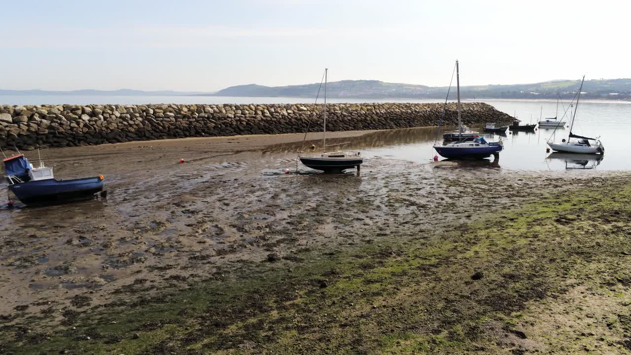 Aerial view boats in shimmering low tide sunny warm Rhos on Sea rock jetty seaside sandy beach marina orbit left low
