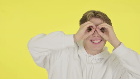 young man searching with handmade binocular on yellow screen