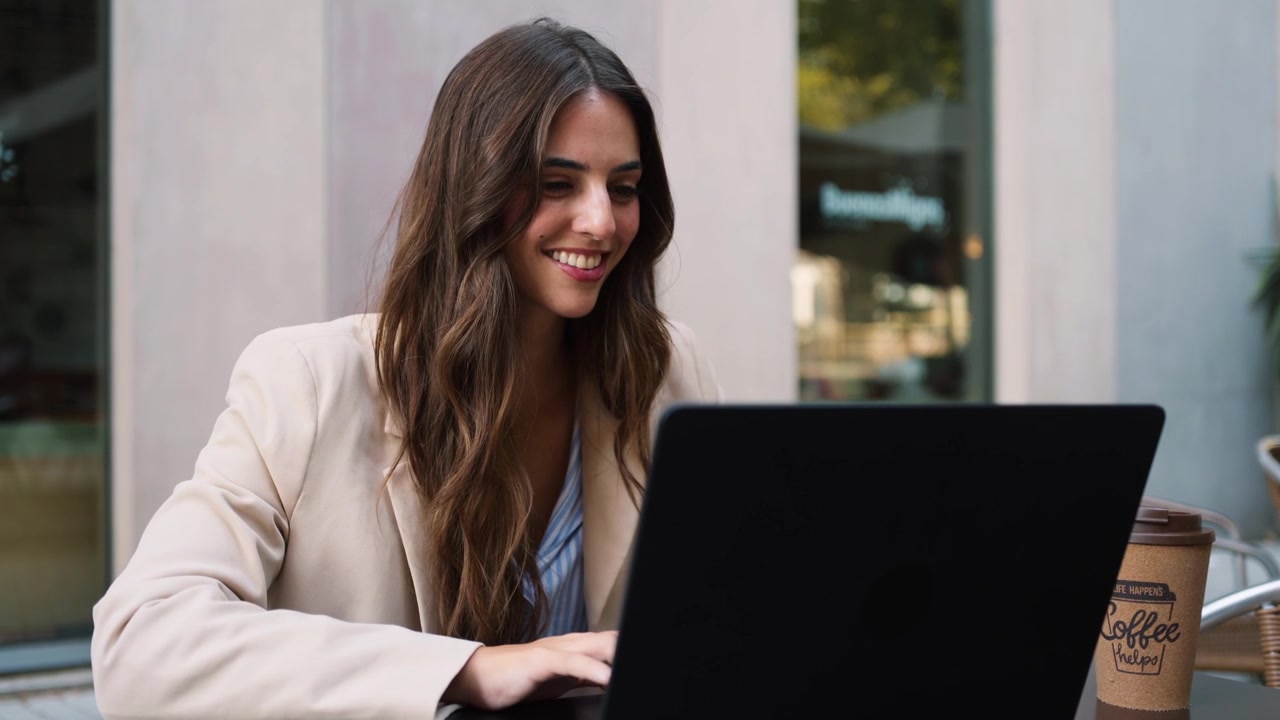 Mujer joven trabajando en una computadora portátil en un café al aire libre