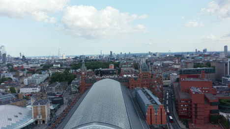 Backwards-fly-above-large-building-of-St-Pancras-train-station.-Aerial-view-of-roof-over-platforms-in-transport-terminal.-London,-UK