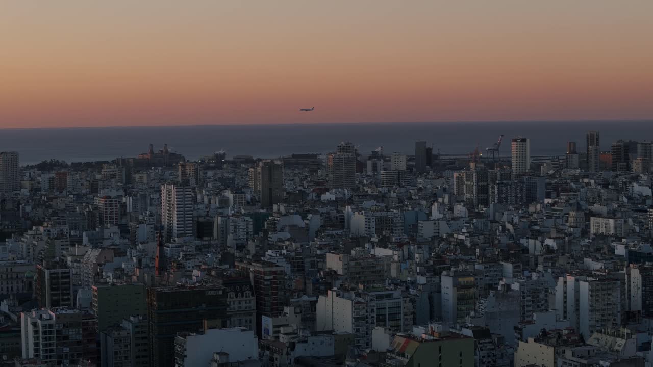 Drone telephoto shot of Buenos Aires cityscape during sunset, with airplane flying over the skyline