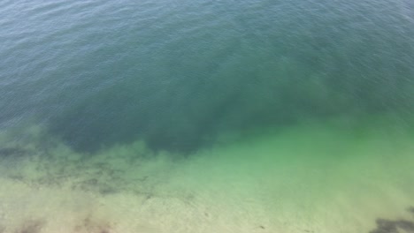 Drone-aerial-spinning-over-pristine-blue-beach-with-white-sand