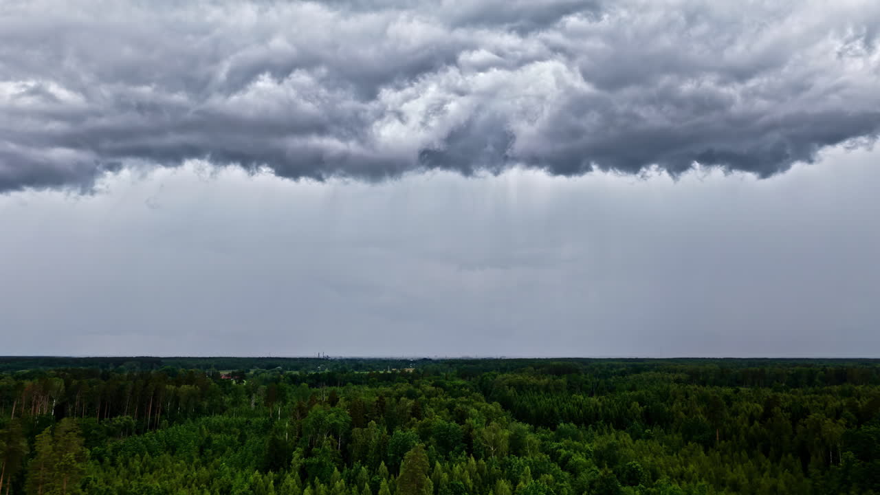 A dramatic aerial parallax shot reveals dark storm clouds rolling above a lush green forest near Jelgava, Latvia