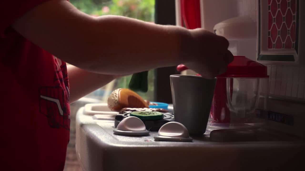 Young toddler boy playing with toy kitchen and food in front of sunny window