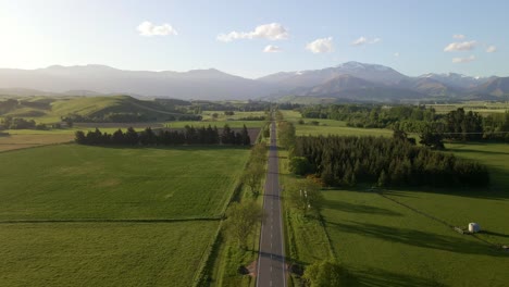Aerial-dolly-out-over-a-straight-picturesque-countryside-highway-with-spectacular-mountain-views-at-sunset