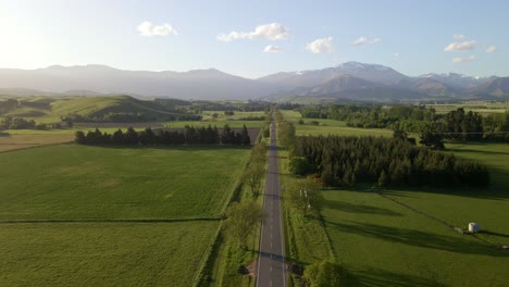 aerial dolly out over a straight picturesque countryside highway with spectacular mountain views at sunset