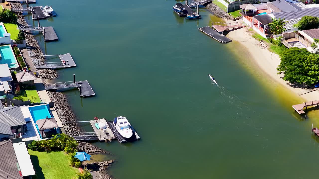 Góc quay từ trên cao của một người đang chèo thuyền kayak lướt qua những ngôi nhà ven sông sang trọng