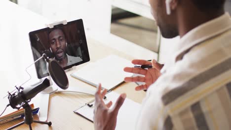 Happy-african-american-man-sitting-at-table-in-kitchen,-using-tablet-and-making-vlog