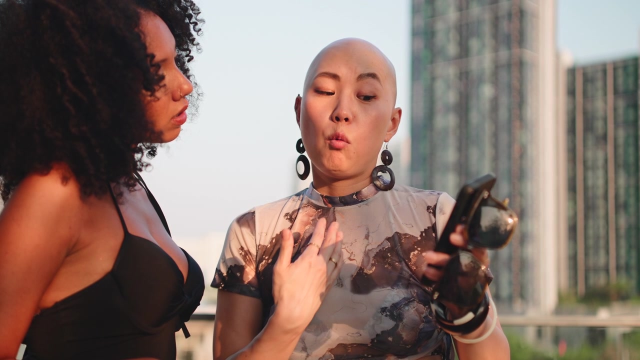 Two Diverse Women Talking and Using Smartphone on Urban Rooftop