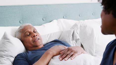 nurse visiting senior man lying in bed suffering with illness