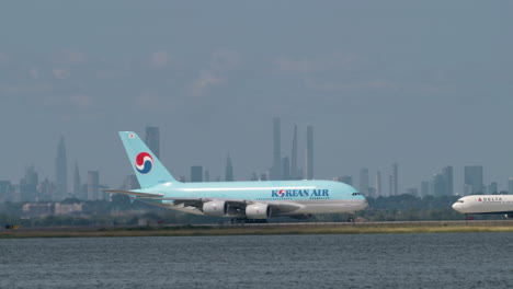 korean air passenger plane taxis on runway at jfk airport with manhattan skyline in distance on hazy day