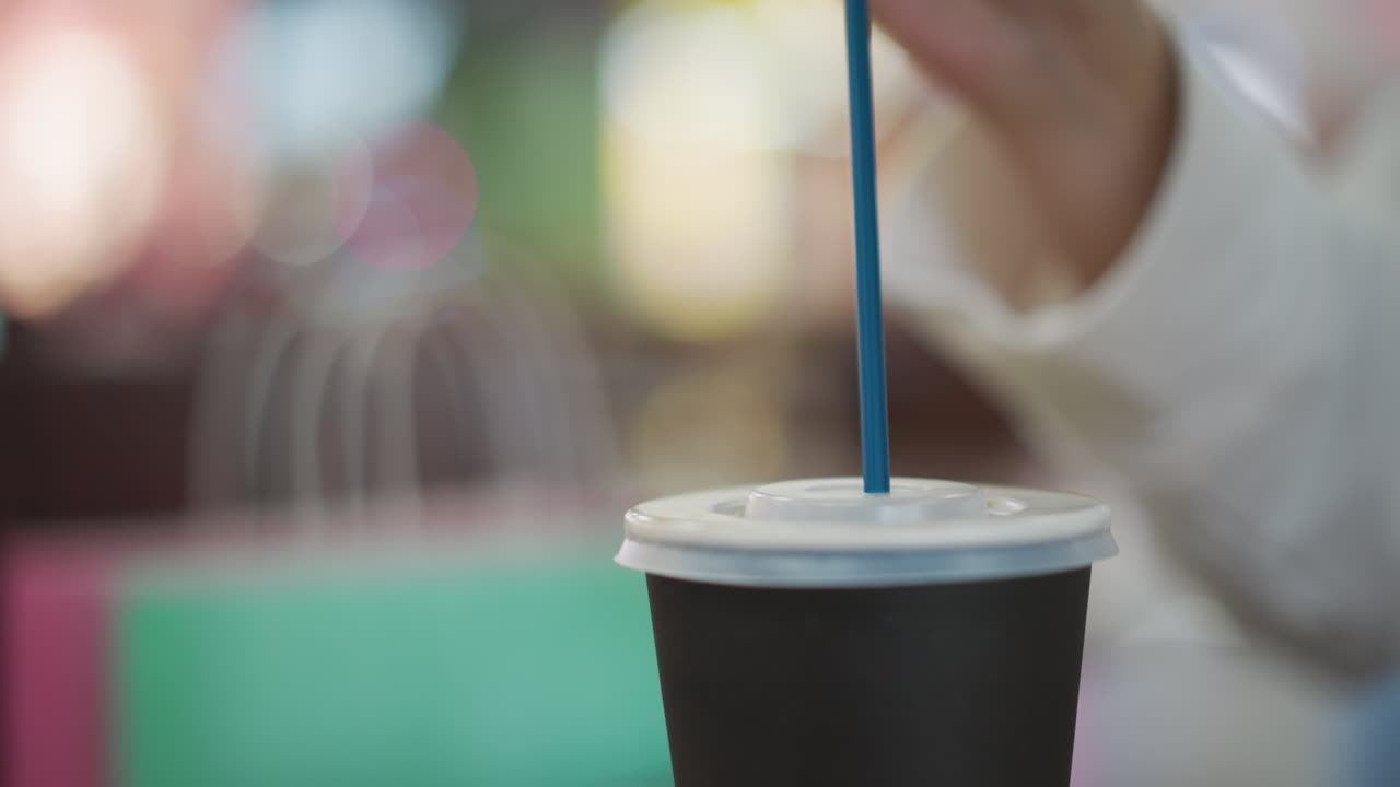 primer plano de la mano insertando suavemente una pajita negra en la tapa de una taza de té para llevar, creando una escena minimalista con un fondo borroso suave y luces bokeh