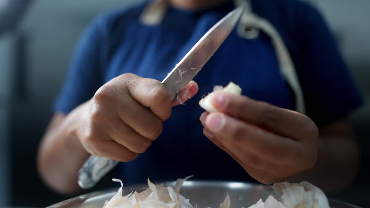 Close up cinematic view of two hands peeling garlic with a knife in a restaurant kitchen.