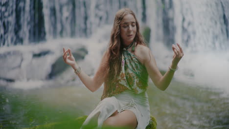 view of a beautiful woman meditating in the middle of the forest in front of a waterfall