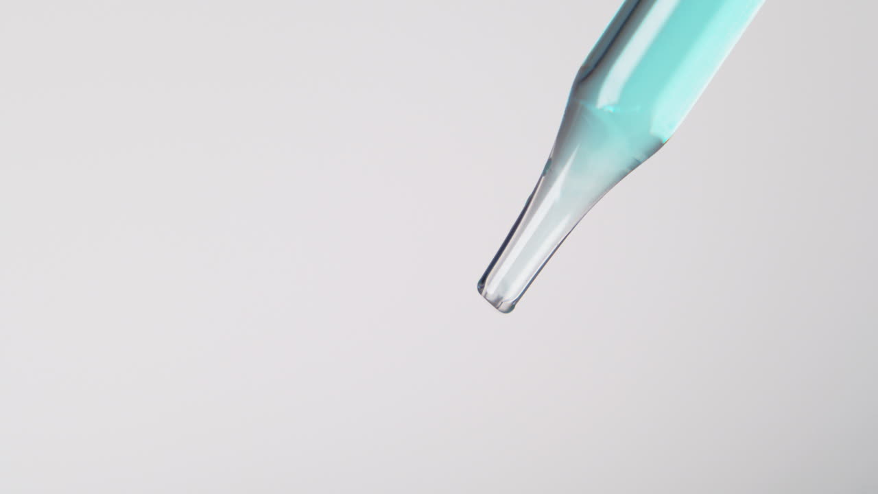 A blue liquid slowly dripping from a pipette, close shot