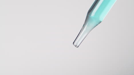 A-blue-liquid-slowly-dripping-from-a-pipette,-close-shot