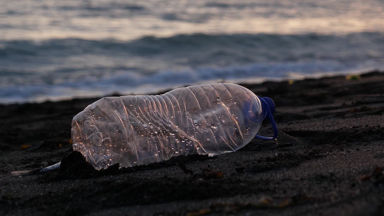 una botella de plástico desechada en una playa de arena al atardecer