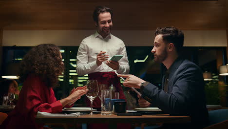 smiling waiter serving couple on restaurant date. mixed race lovers in cafe bar.