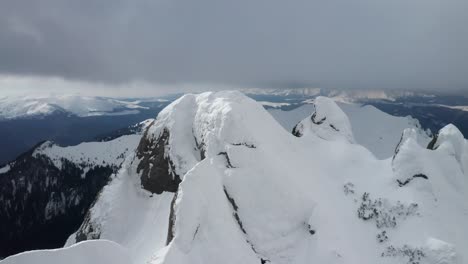 Snow-capped-Tigaile-Mari-Peak-in-Ciucas-Mountains-under-cloudy-skies,-expansive-view