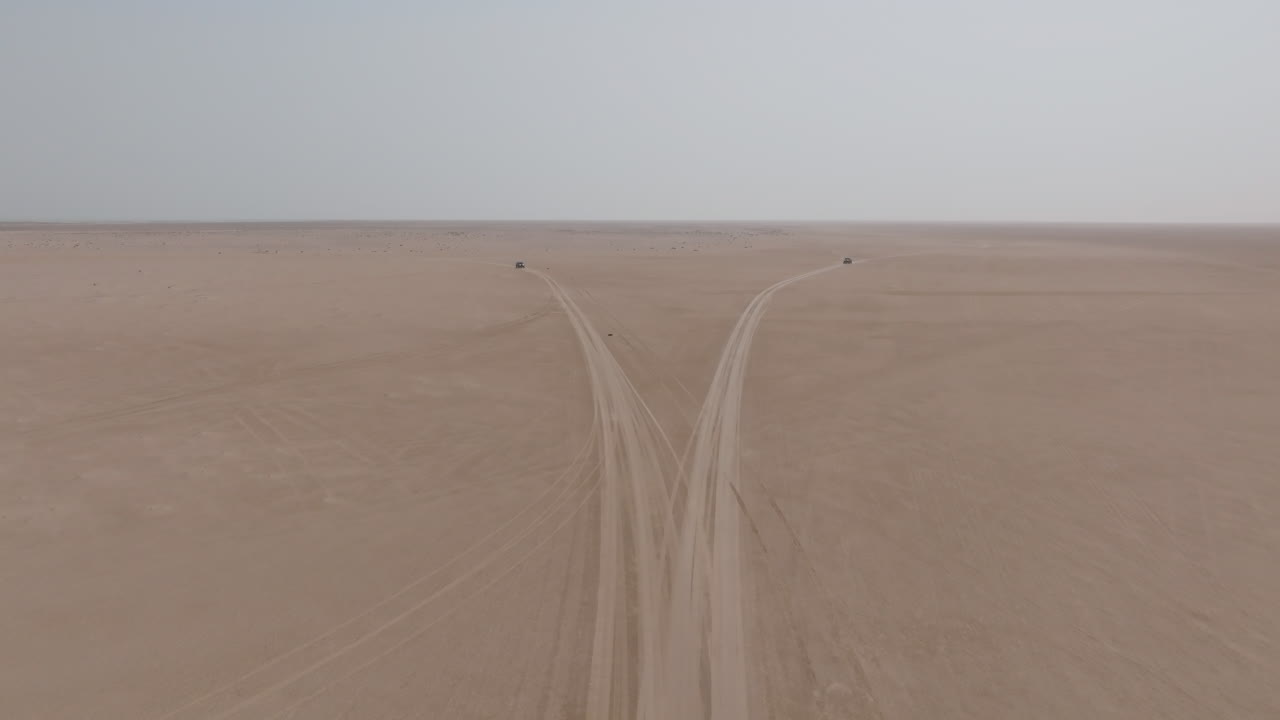 Two 4x4 vehicles split on desert tracks toward Bar Al Hikman, Oman, aerial view